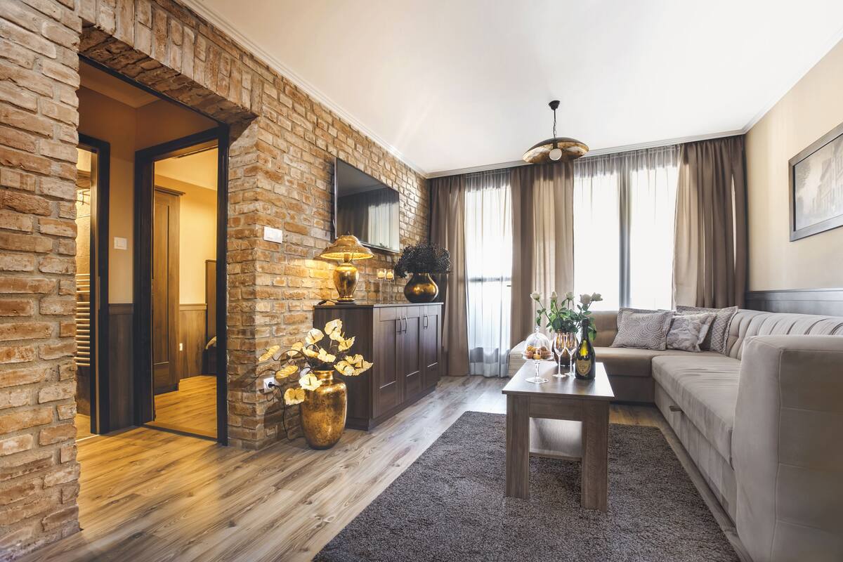 Una sala de estar con pared de ladrillo, suelo de madera, un sofá, una mesa de centro y un televisor.