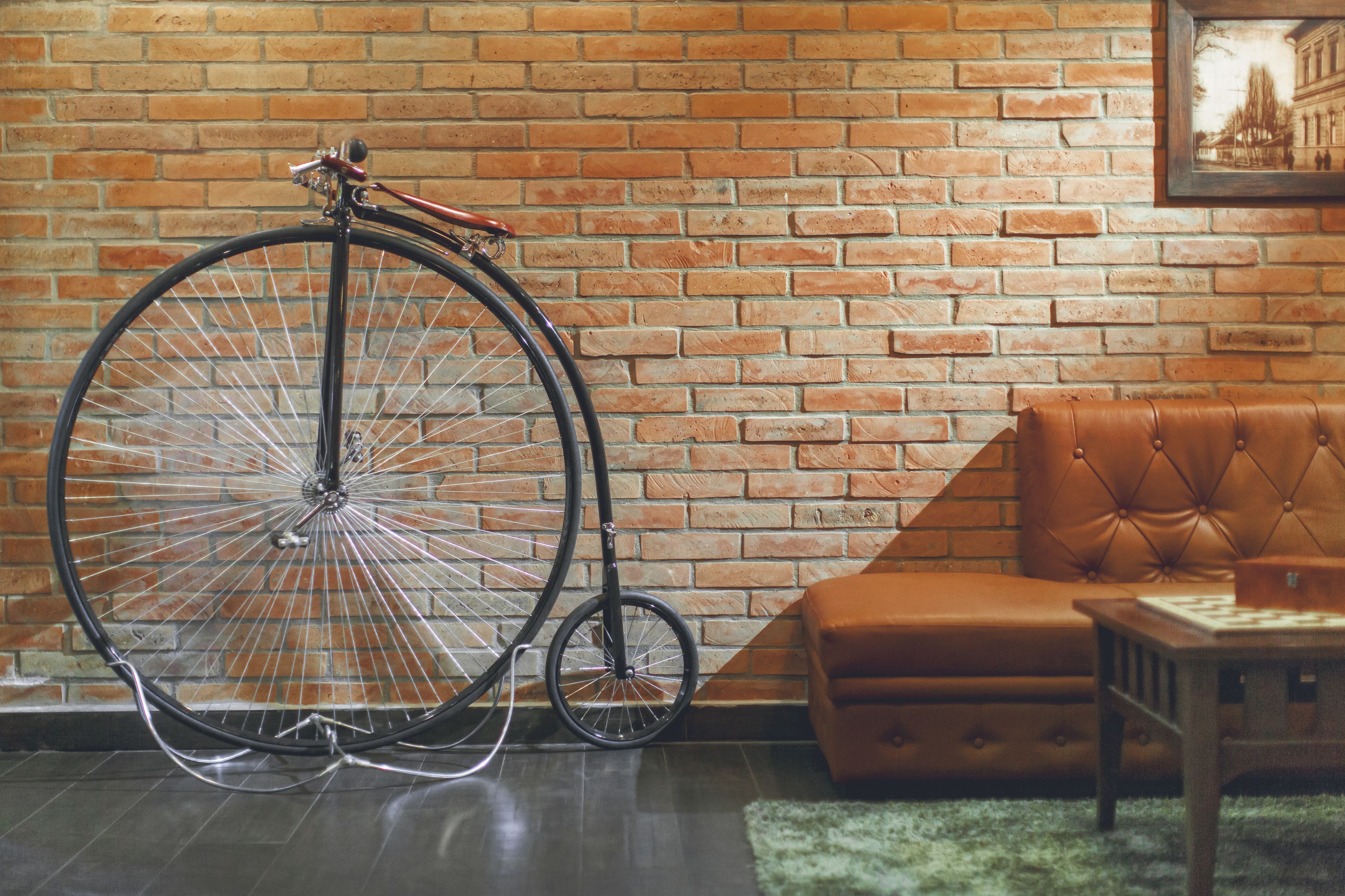 Ein Zimmer mit Backsteinwand, einem großen Fahrrad, einer braunen Ledersofa und einem kleinen Holztisch.