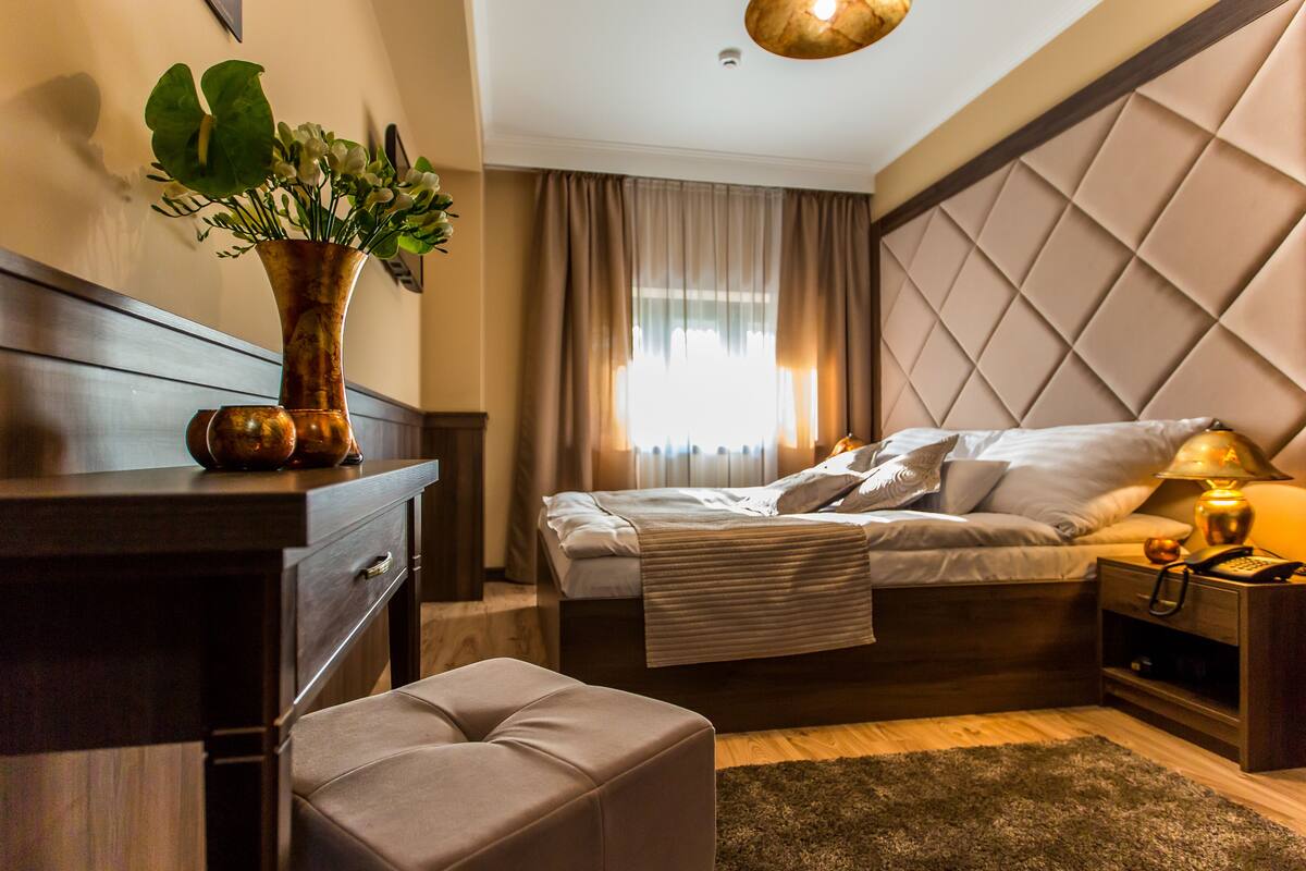 Un dormitorio moderno con cama, mesita de noche, lámpara y un jarrón decorativo con flores.