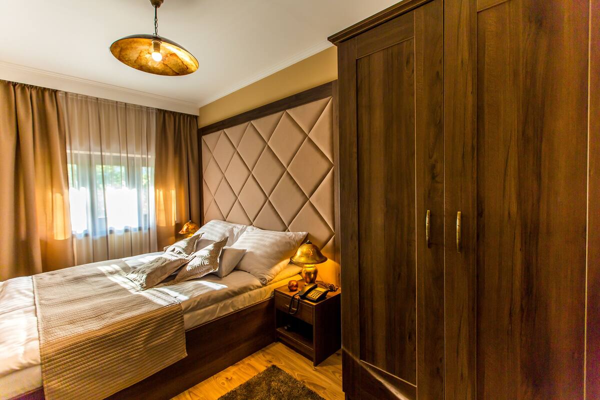 Un dormitorio con cama, mesita de noche, lámpara, armario y una lámpara colgante.