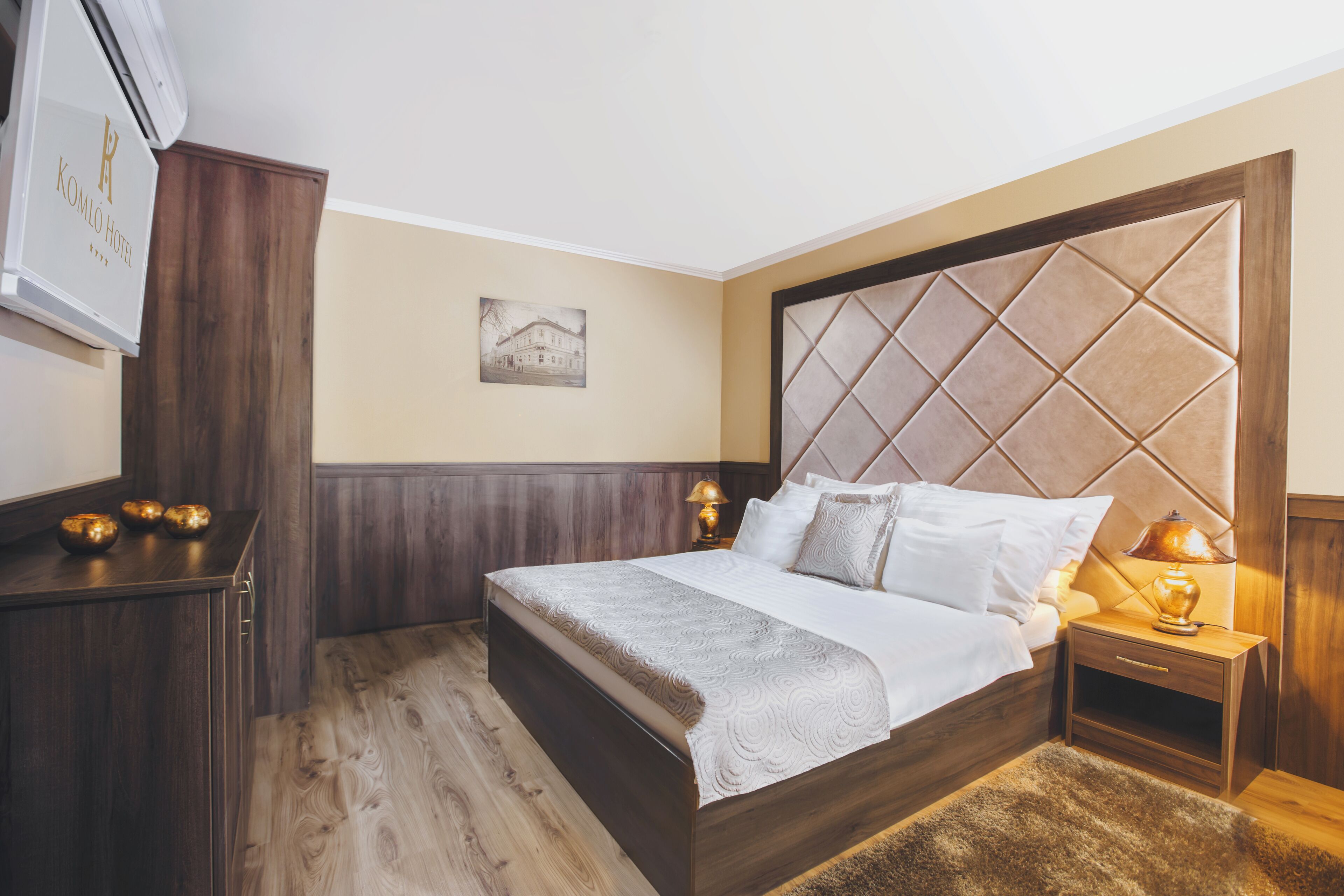 Habitación de hotel con una cama grande, cabecera de madera, una mesita de noche con lámpara y aire acondicionado instalado en la pared.