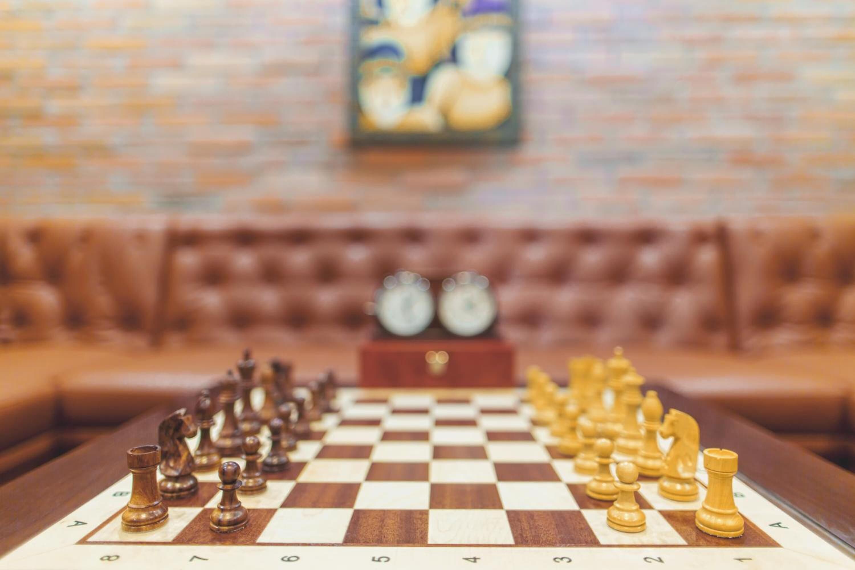 A chessboard set up on a table with a clock in the background.