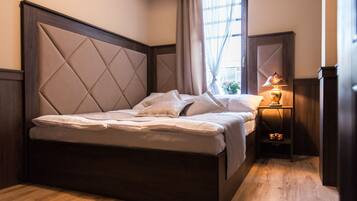 Una cama bien hecha con cabecera de madera, una mesita de noche con lámpara y una ventana con cortinas.