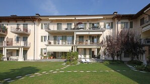 A multi-story building with balconies, a central courtyard with lounge chairs, and potted plants. - Il Cedro (Salò)