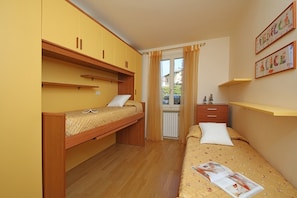 Habitación pequeña con dos literas, un escritorio y ventana con cortinas.