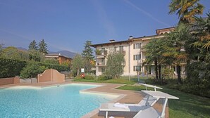 A swimming pool with lounge chairs and a lifebuoy, surrounded by greenery and buildings. - Il Cedro (Salò)