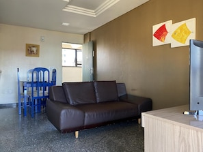 A room with a brown leather sofa, a blue chair, a wooden desk, and two wall-mounted paintings.