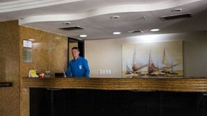 Eine Rezeption mit einem dahinter stehenden Mann, ein Segelbootgemälde an der Wand und ein Schwarzes Brett mit einer Mitteilung.