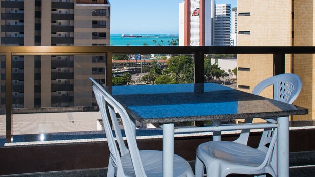 Ein Balkon mit Tisch und Stühlen, der auf eine Stadtansicht und ein Gewässer blickt.