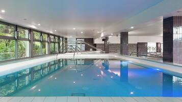 An indoor swimming pool with clear glass walls, a tiled floor, and a staircase leading to a higher level.