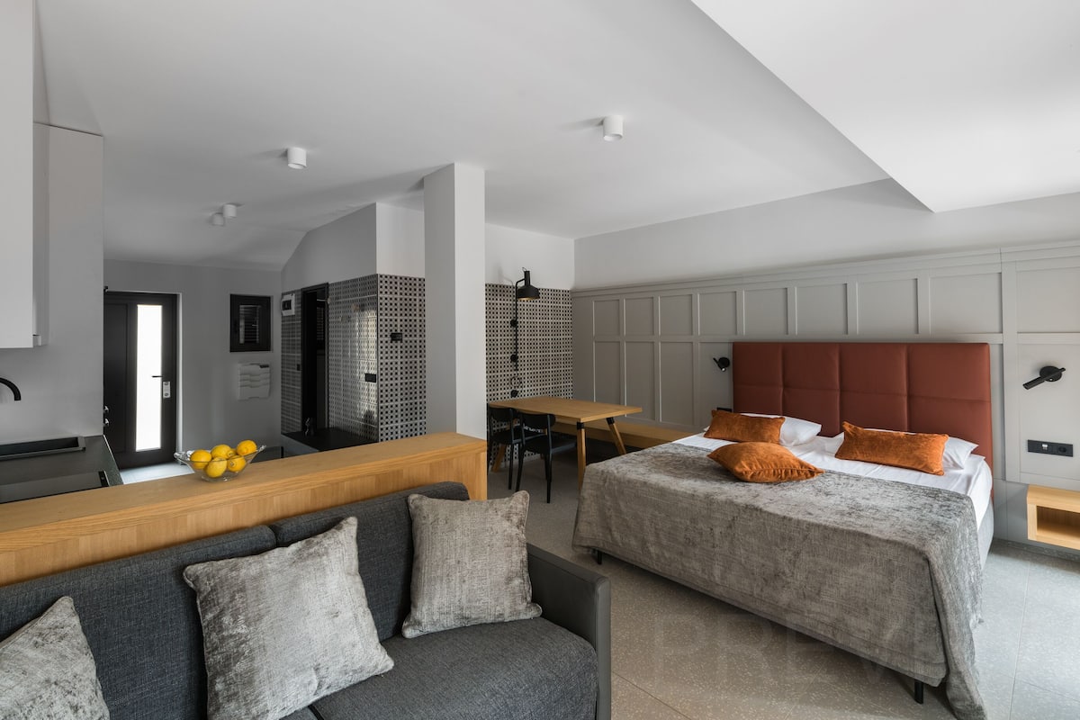 Una habitación de hotel moderna con sofá, dos camas, una mesa de comedor y una zona de cocina.