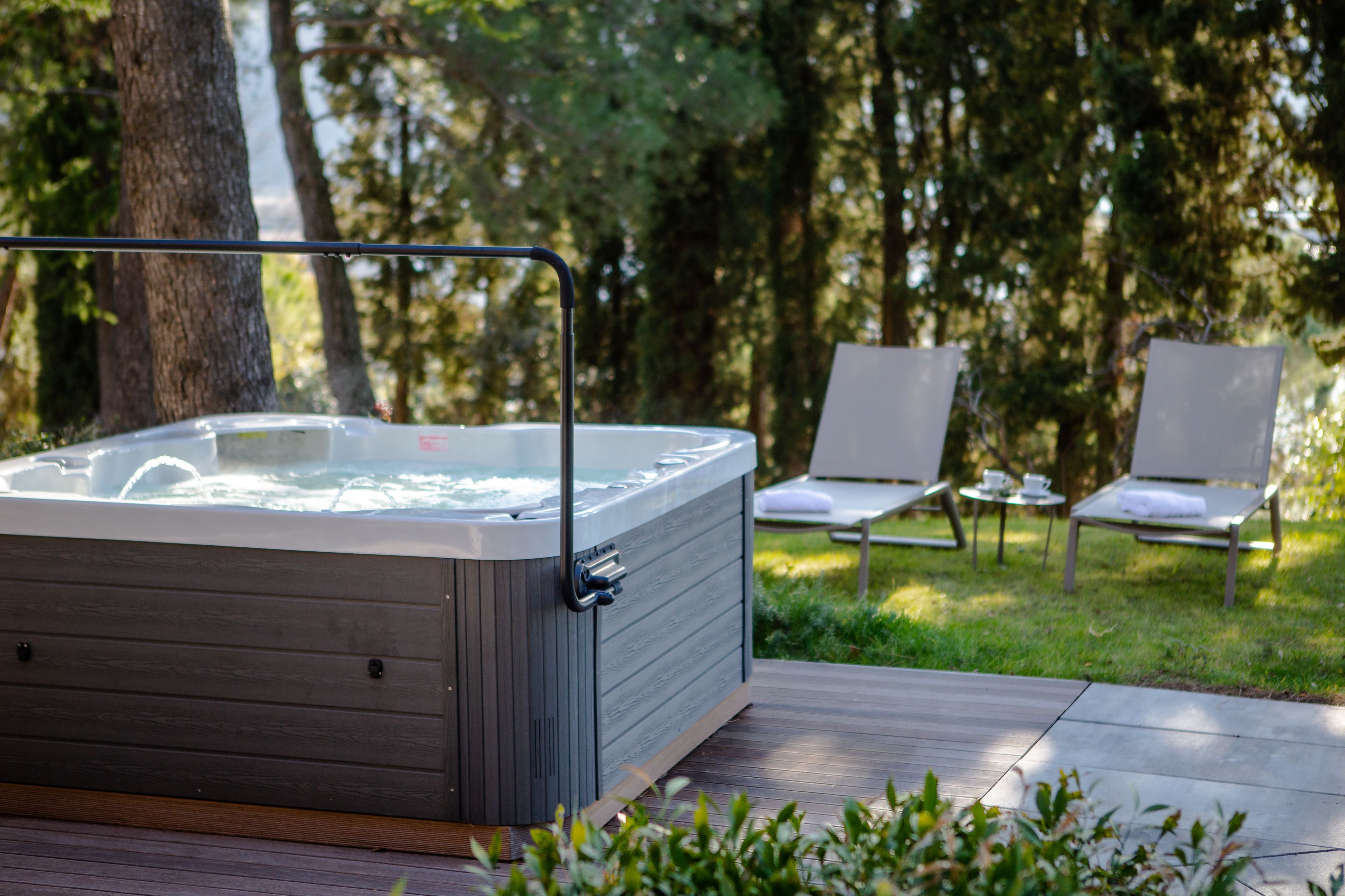 A hot tub on a wooden deck with a grassy area and lounge chairs in the background.