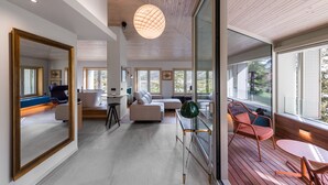 Un interior moderno con un espejo grande, una zona de estar con sofá y sillones, una mesa redonda y vistas amplias a través de grandes ventanales.