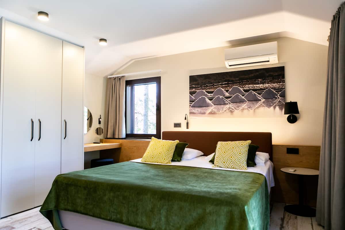 Habitación de hotel con cama, escritorio, armario, ventana y aire acondicionado instalado en la pared.