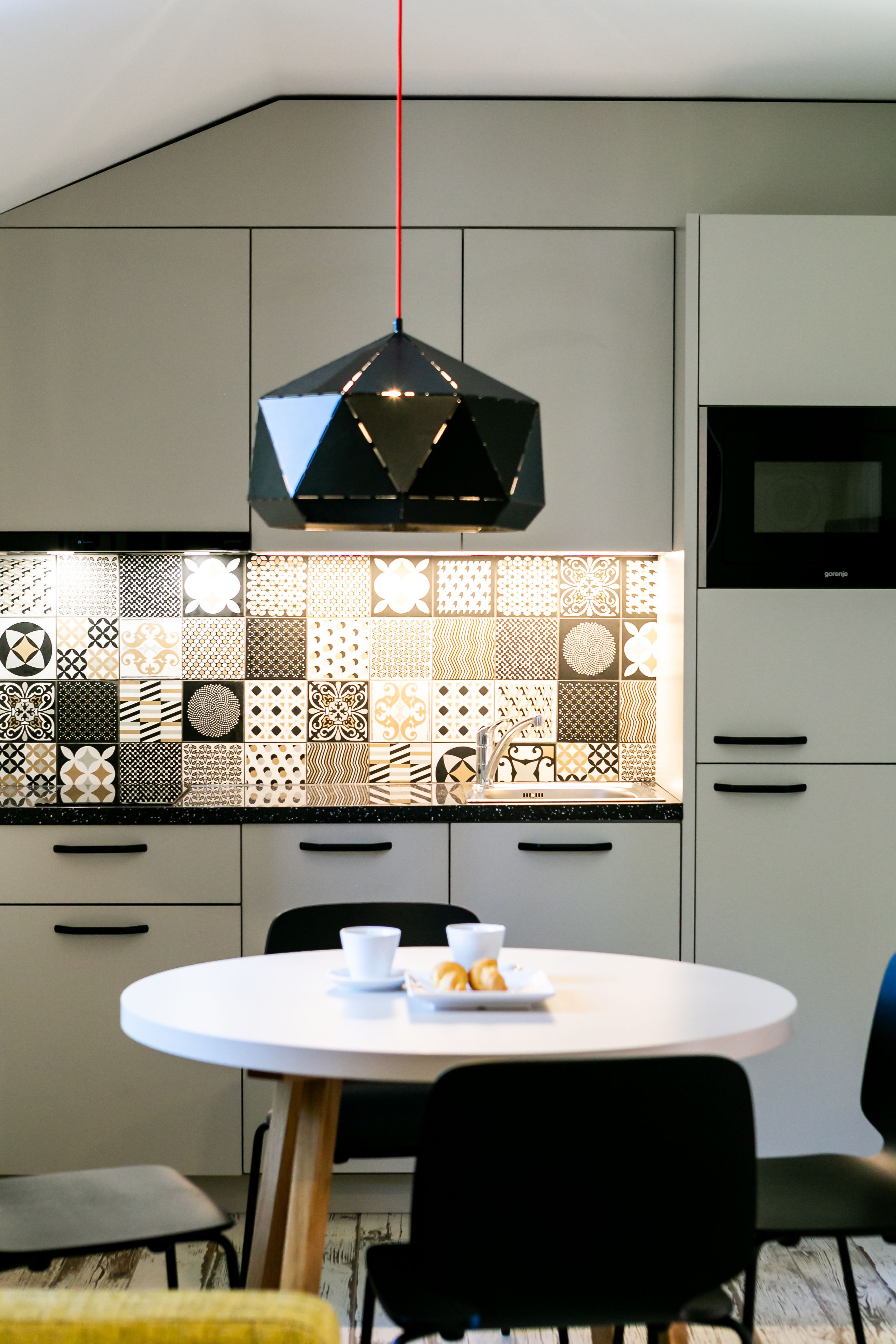 Una cocina moderna con un original mosaico de pared, una mesa redonda para comer y una lámpara colgante.