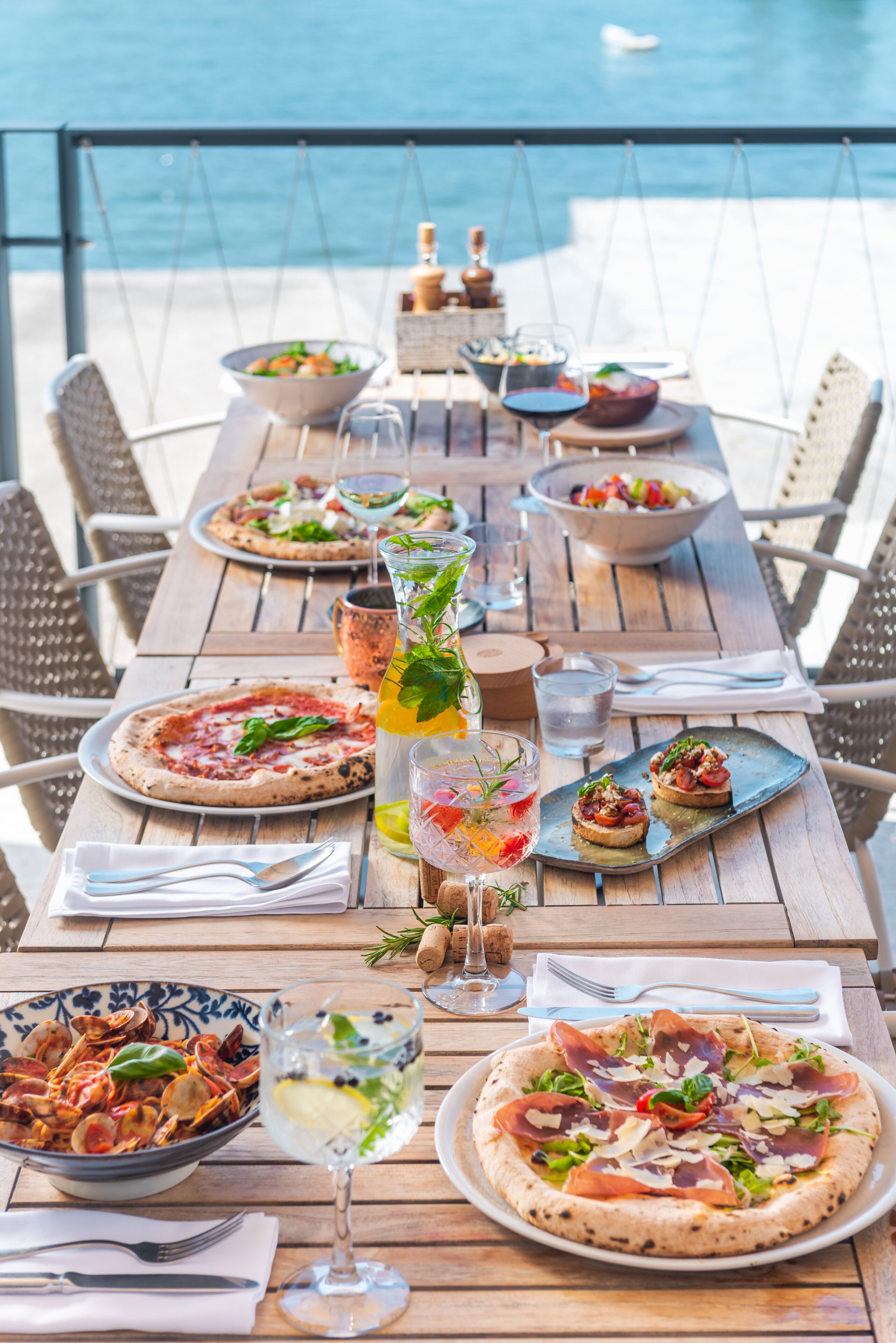 A wooden dining table with various dishes, including pizzas and salads, set for a meal.