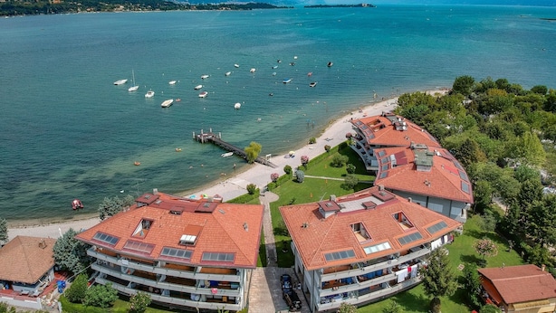 A coastal hotel with multiple balconies, a dock, and a view of the sea and mountains. - Il Sogno del Lago (Manerba del Garda)