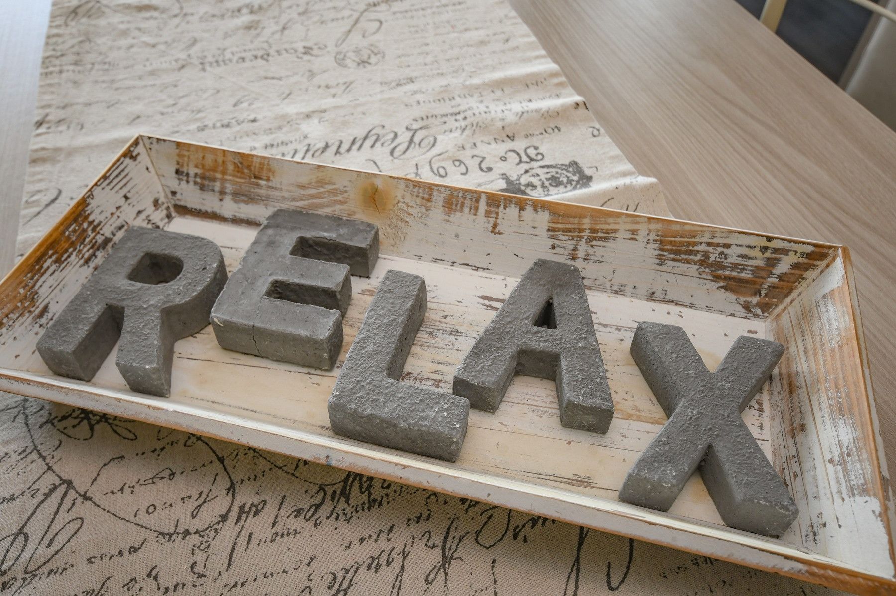 A rustic wooden tray with the word "RELAX" spelled out in concrete blocks.