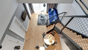 A modern interior with a dining area featuring a round table and chairs, a blue sofa, and a staircase with a metal railing. - Equus Apartments (Sopot)