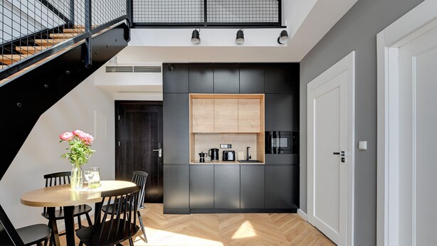 A modern kitchen with a herringbone floor, a dining area with a round table and chairs, and a staircase with a black railing. - Equus Apartments (Sopot)