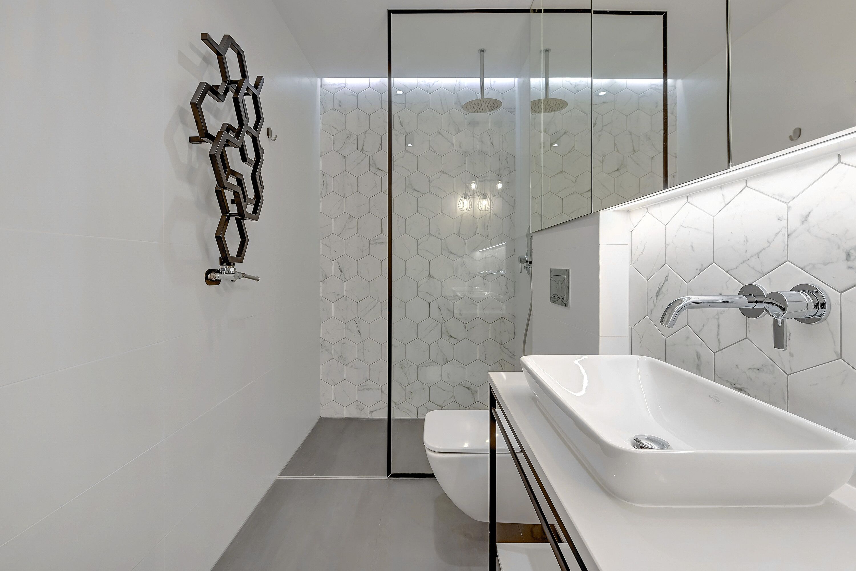 A modern bathroom with a white sink, a glass shower enclosure, and a hexagonal tile backsplash.