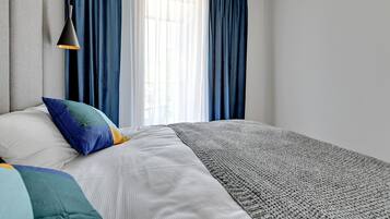 A bedroom with a bed, pillows, a blanket, a hanging lamp, and a window with curtains.