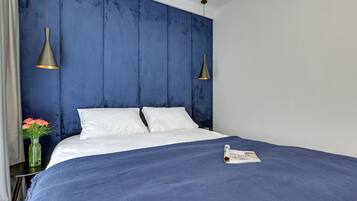 Una cama bien hecha con sábanas blancas, una colcha azul y dos lámparas colgantes.
