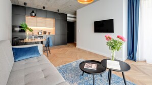 A modern living room with a grey sofa, a coffee table, and a dining area with a kitchen in the background. - Equus Apartments (Sopot)
