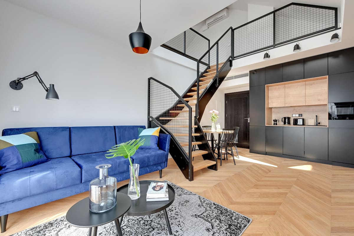 A modern living room with a blue sofa, a black coffee table, and a staircase leading to an upper level.