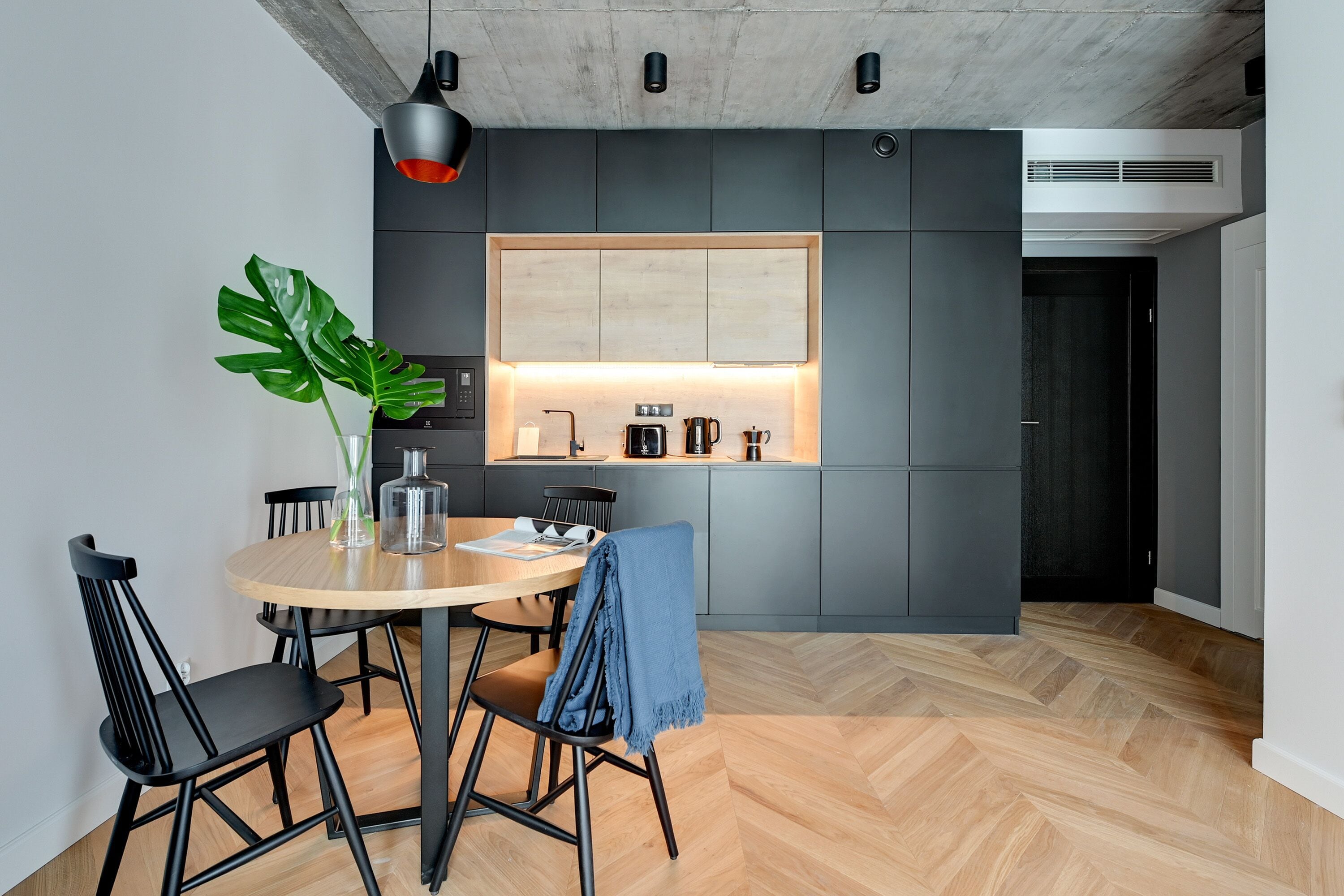 A modern kitchen with a wooden dining table, black chairs, and a potted plant.