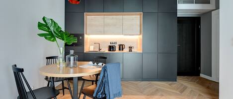 A modern kitchen with a wooden dining table, black chairs, and a potted plant.