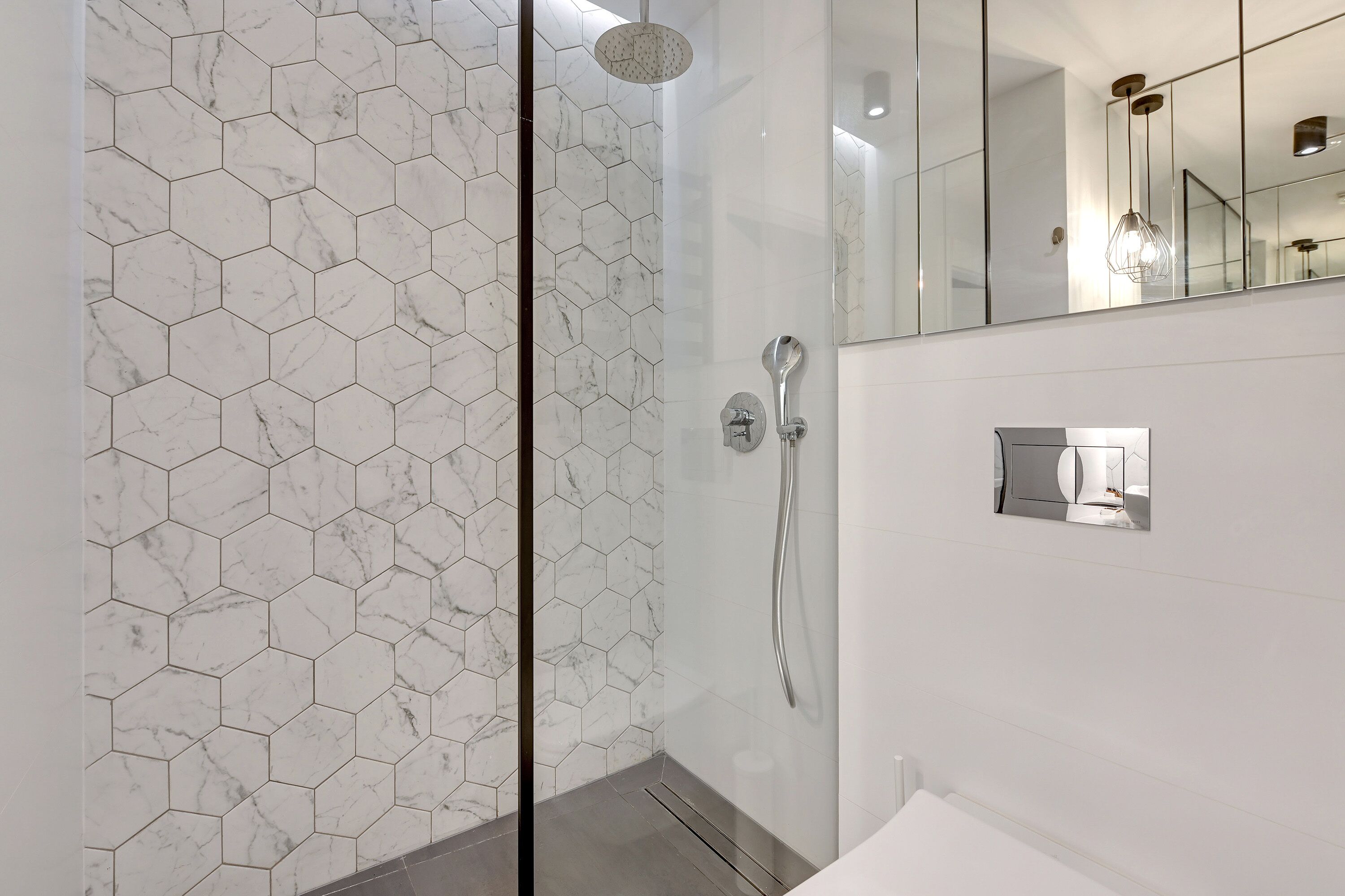 Une salle de bain moderne avec un carrelage à motifs hexagonaux, une douche en verre et un grand miroir.
