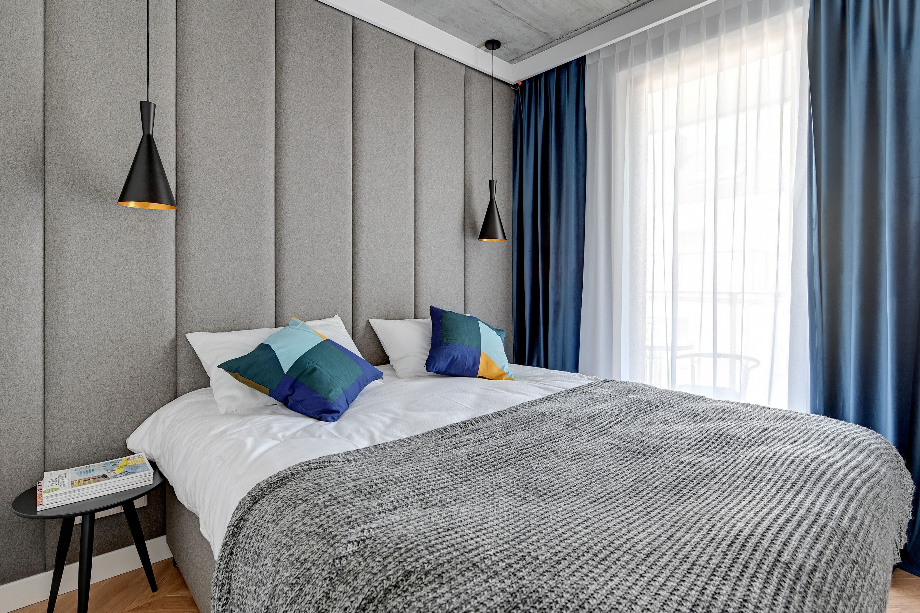 Ein modernes Schlafzimmer mit einem großen Bett, grauen Wänden und zwei Pendelleuchten.