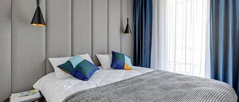 Ein modernes Schlafzimmer mit einem großen Bett, grauen Wänden und zwei Pendelleuchten.