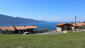 A coastal view with terracotta-roofed buildings, a clear blue sky, and a body of water in the distance. - Infinity (Tignale)