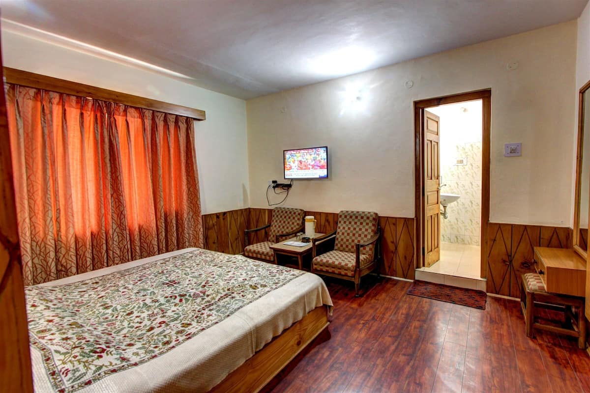 A bedroom with a large bed, two chairs, a small table, and a television on the wall.