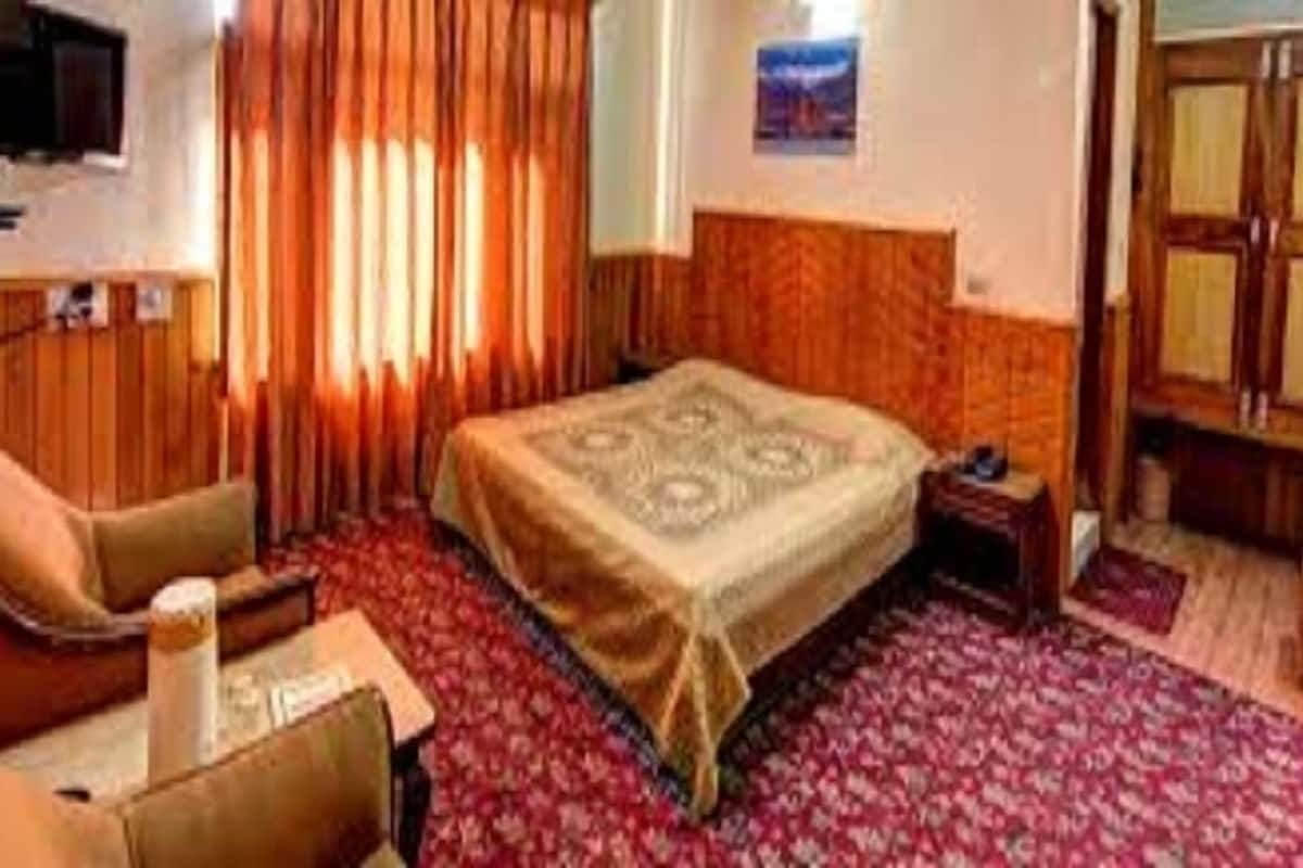 A hotel room with a bed, a chair, a small table, and a television.