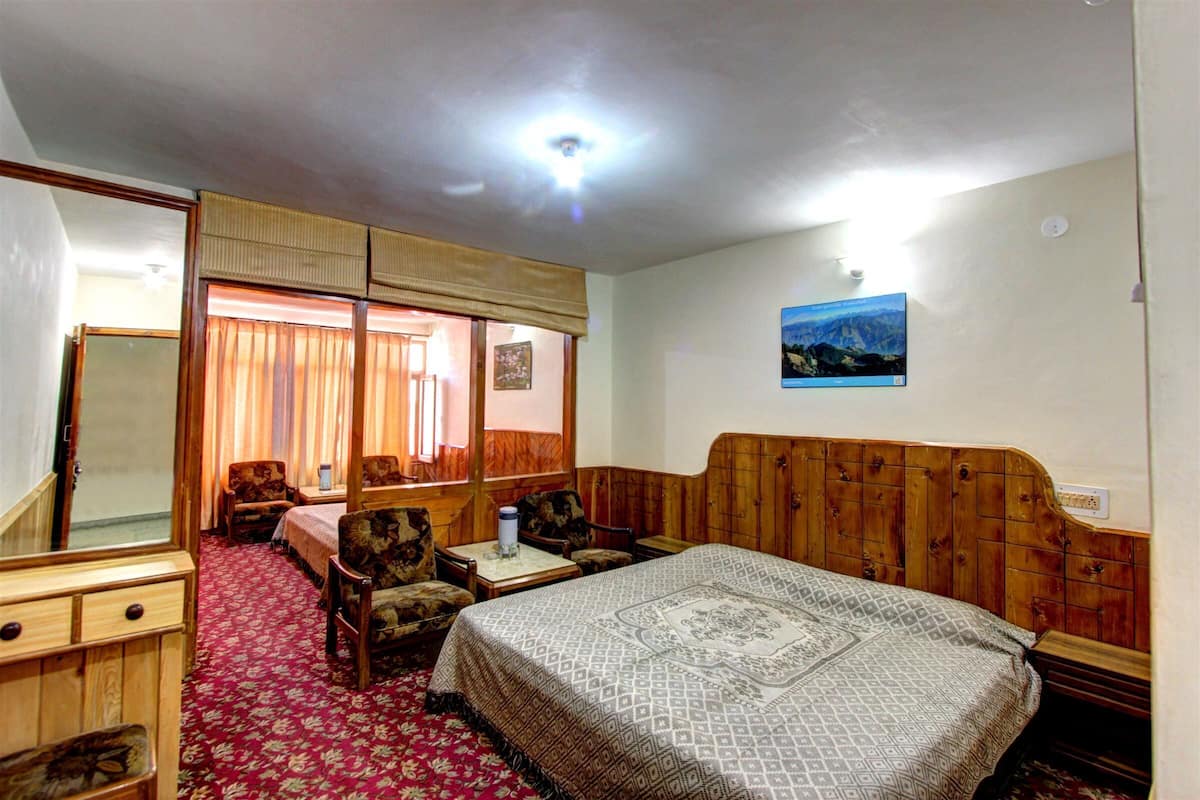 A hotel room with a bed, two chairs, a small table, a mirror, and a picture on the wall.