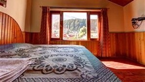 Une chambre avec un grand lit, des murs en bois et une fenêtre donnant sur une zone boisée.