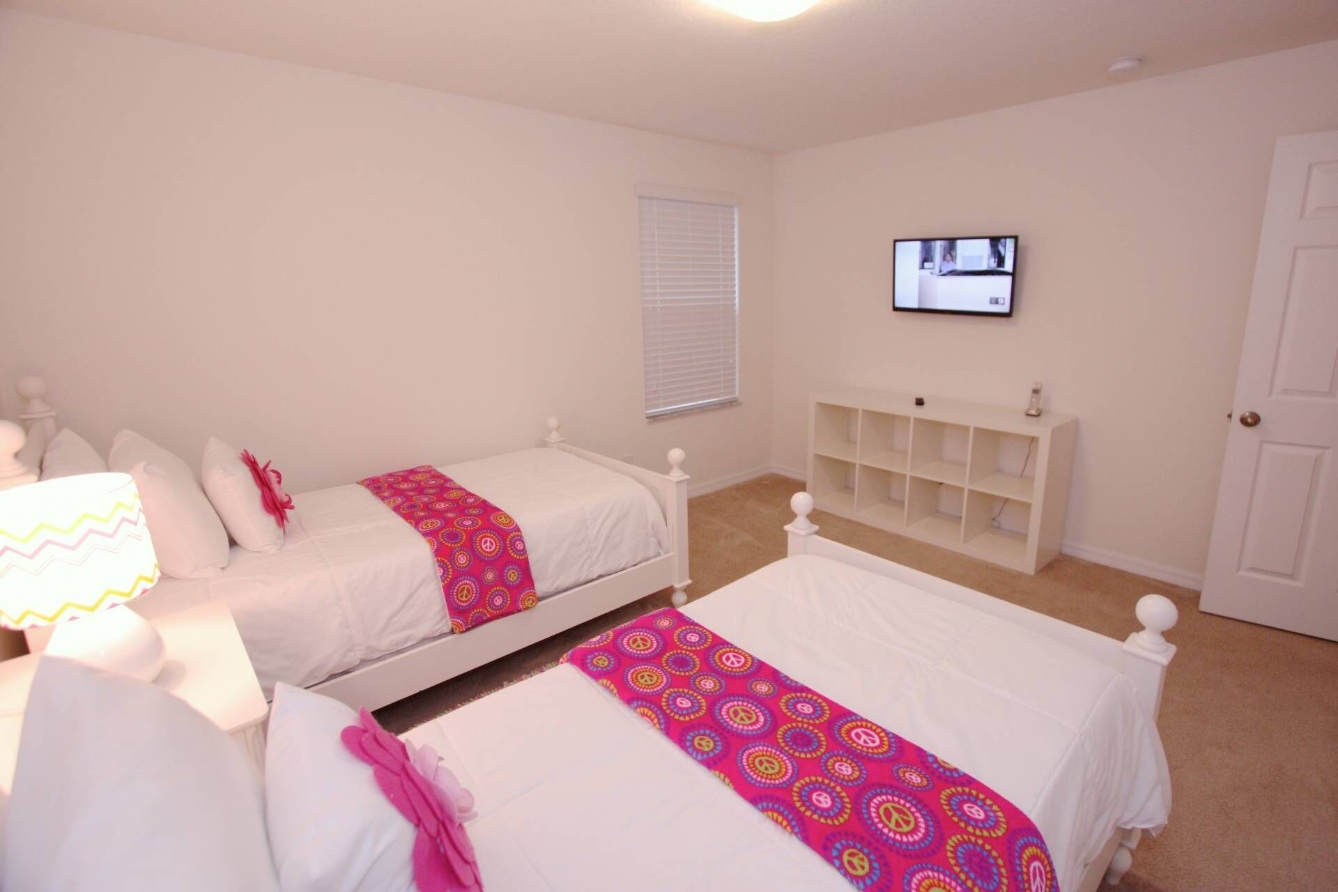 Un dormitorio con dos camas individuales, un televisor instalado en la pared y un estante blanco.