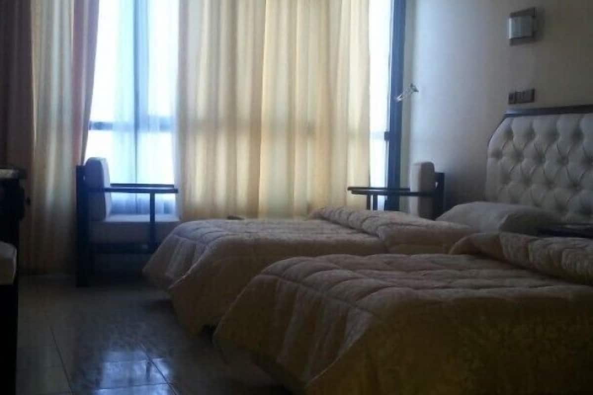 Ein Hotelzimmer mit zwei Betten, einem Schreibtisch, einem Stuhl und einem fenster mit Vorhängen.
