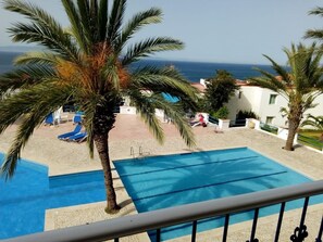 Un área de piscina con palmeras, sillones de descanso y vista al mar.