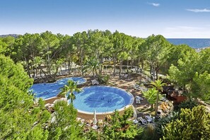 A resort with multiple swimming pools surrounded by lush greenery and palm trees, overlooking a body of water. - Palmira Beach Hotel (Calvia)