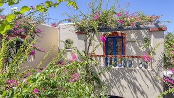 A building with a balcony, surrounded by lush greenery and pink flowers.