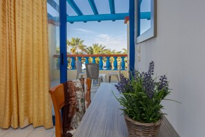 A balcony with a wooden table, chairs, and a potted plant. - Palm Bay (Agios Nikolaos)
