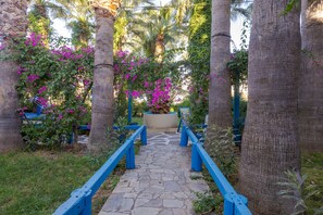 A stone pathway flanked by blue railings leading to a seating area with a bench and a planter with pink flowers. - Palm Bay (Agios Nikolaos)