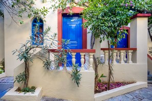 A building with a blue door and a blue window, surrounded by plants and a white balcony. - Palm Bay (Agios Nikolaos)