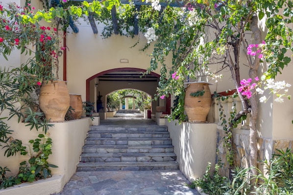 A stone staircase leading to an arched entrance, surrounded by lush greenery and large terracotta pots. - Palm Bay (Agios Nikolaos)