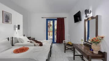 A hotel room with two beds, a desk with a mirror, a chair, a small table with a vase of flowers, and a TV mounted on the wall.