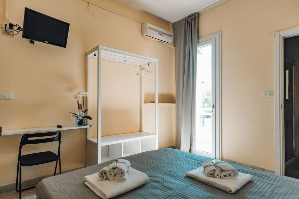 A hotel room with a bed, a desk, a chair, a TV, and a wardrobe.